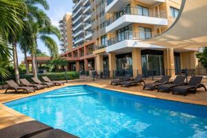 a swimming pool with lounge chairs and a building at Esplanade 88 in Darwin
