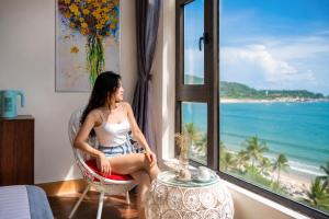 a woman sitting in a chair looking out a window at the beach at Sontra Sea Hotel in Danang