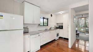 a white kitchen with white appliances and wood floors at Quirky and Captivating Kurra in Hawks Nest