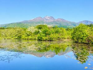a reflection of trees and mountains in a lake at Komorebi Myoko Lodge in Myoko
