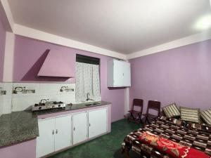 a room with purple walls and a kitchen and a bed at itynnad homestay in Shillong