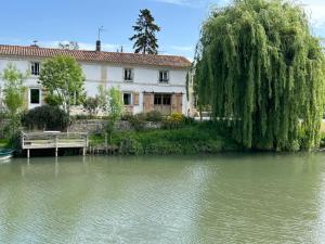 a house sitting next to a river with a tree at Double chambres hôtes parentales in Damvix