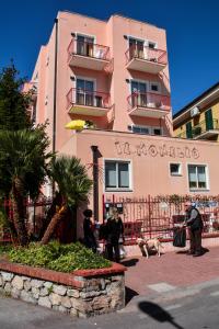 un grupo de personas de pie fuera de un edificio rosa en Residence Il Monello, en Loano