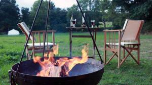 a fire pit with two chairs and a table with wine glasses at La Toile sous Les Étoiles in Charron
