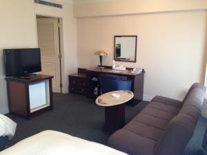ein Hotelzimmer mit einem Sofa, einem Schreibtisch und einem TV in der Unterkunft Creston Hotel in Iwaki