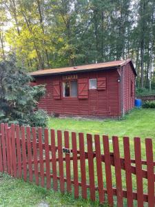 a red house with a fence in a yard at Merylula - Domek nad jeziorem in Przydwórz