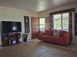 a living room with a red couch and a flat screen tv at Yaubula Bed and Breakfast Homestay in Nadi