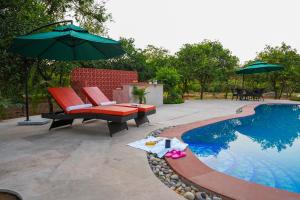 a patio with two chairs and an umbrella next to a pool at Orchard At Sarai - Luxury Tent Villas, Swimming Pool, Large lawns, & Pet friendly in Gurgaon