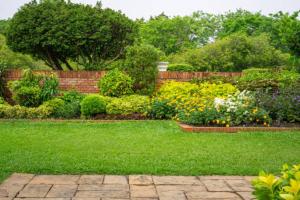 a garden with green grass and flowers and a brick fence at De Villione Guesthouses in Bultfontein