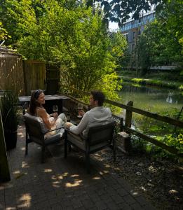 a man and woman sitting in chairs next to a pond at 1 bed flat, free parking, canalside, sleeps 2 in Hertford