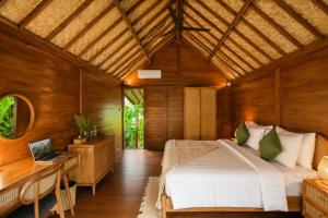 a bedroom with a bed and a desk with a laptop at The Payung House - Romantic Riverside Villa in Bebandem