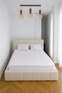 a white bed in a white bedroom with two lights at Ayan Băile Felix Apartament in Baile Unu Mai