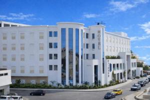 a white building with cars parked in a parking lot at Hotel Maamoun in Gafsa