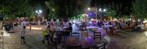 a crowd of people sitting at tables in a street at night at George's house samos in Pagóndas