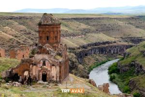 an old building on a hill next to a river at David Moser 1878 Oteli in Kars