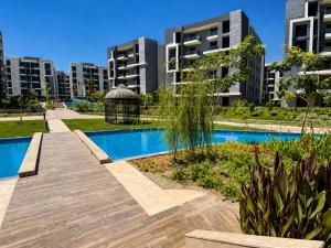 a swimming pool with a wooden walkway in front of buildings at Cyra gate Suncapital compound شقة في كامبواند صنكابيتال بوابة كايرا بالقرب in ‘Ezbet `Abd el-Ḥamîd