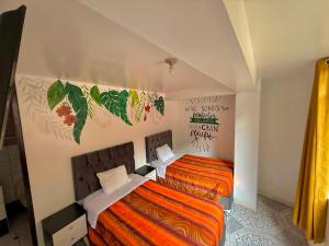 a bedroom with two beds with orange sheets and a painting on the wall at Hostal Mónaco in Machu Picchu