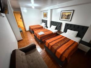 a room with three beds and a chair in it at Hostal Mónaco in Machu Picchu