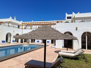 a large straw umbrella sitting next to a pool at Villa Daba By Zelia in Ghazoua