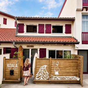 a woman standing in front of a house with a surfboard at Koala Surf House, en bord d'Océan, planches de surf et skates à disposition in Hossegor
