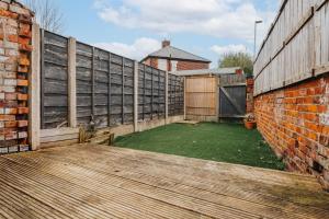 a garden with a wooden deck and a brick wall at Denton Luxury Home - Sleep 8 - Speedy Wi-Fi - Free On-Site Parking in Denton
