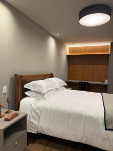 a bedroom with a bed with white sheets and a light at Apartamento Boutique Cheia de Graça 304 in Divinópolis