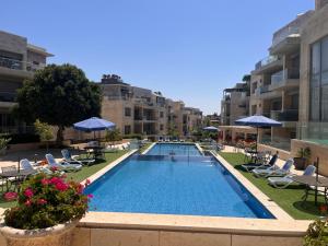 a swimming pool with chairs and umbrellas in a building at Spacious Abdoun 2BR with private garden & pool access in Amman