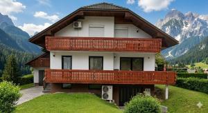 a house with a balcony on a hill with mountains at Apartma Tri Planike in Mojstrana