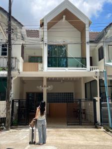 a woman standing in front of a house with a suitcase at The Kanee Hostel in Nakhon Phanom