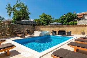 a swimming pool with chairs and umbrellas in a backyard at Villa Sagri - heated pool in Žagrići