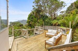 a wooden deck with a couch and chairs on it at Sunbird House Piha in Piha