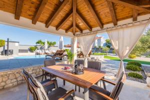a patio with a wooden table and chairs under a wooden roof at Maslina in Vrsi