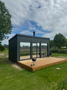a black tiny house with a wooden deck in a field at EstBerg Tartu Glasshouse with Sauna in Tartu