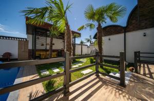 a wooden deck with palm trees and a house at Qafqaz Retro Bungalow in Gabala