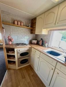 a kitchen with white cabinets and a stove and a sink at Klara Happy Days in Trusthorpe