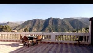 a table and chairs on a balcony with mountains in the background at Gite Tilouguite in Tillouguit nʼAït Isha