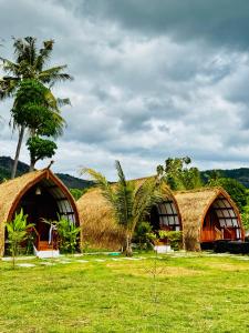two thatched huts with a palm tree in a field at Heyho Bungalow in Maluk