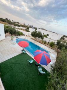 two umbrellas and chairs next to a swimming pool at Villa sedghiani in El Guecheïne