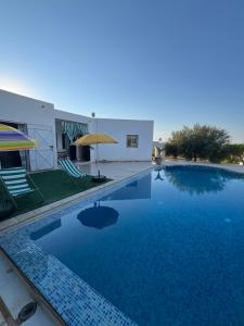 a swimming pool with two chairs and an umbrella at Villa sedghiani in El Guecheïne