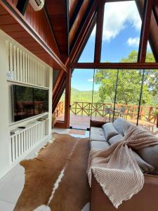 a living room with a couch and a large window at Chalés Aframe com café da manhã artesanal, 39km de Pomerode, Hidromassagem privativa, silenciosos em meio a natureza, lagoa para pesca esportiva in Massaranduba