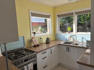 a kitchen with a stove and a sink and two windows at Cute Chartwell Cottage in Hamilton