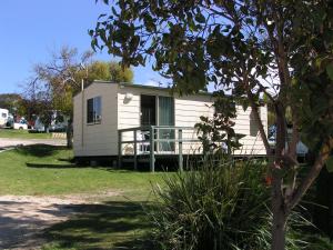 a white tiny house with a porch in a yard at Scamander Tourist Park in Scamander