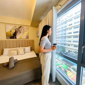 a woman standing in a hotel room looking out the window at 27th Palace at One Manhattan in Bacolod