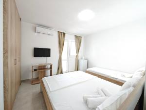 a white bedroom with two beds and a tv at Guest House Violet in Bečići