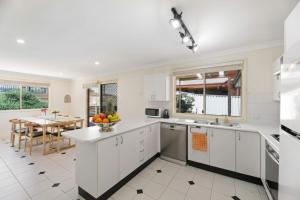 a kitchen with white cabinets and a dining room with a table at Escape from Relaxing Poolside House 3B in Narellan