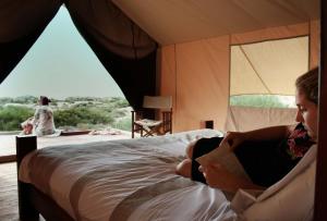 a woman sitting on a bed reading a book at Sal Salis Ningaloo Reef in Exmouth