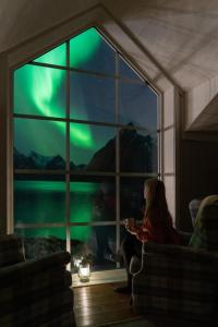a woman sitting in front of a window watching the northern lights at Reinefjorden Sjøhus in Reine