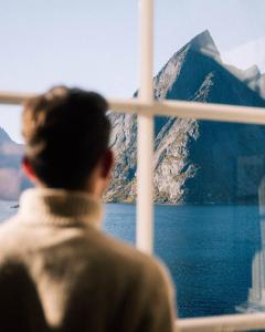 a man looking out a window at a mountain at Reinefjorden Sjøhus in Reine