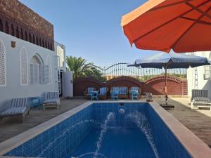 a swimming pool with an umbrella and chairs and a table at Nefertiti Guest House in ‘Ezbet Abu Ḥabashi