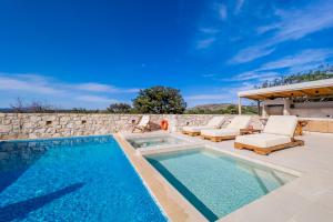 a swimming pool with lounge chairs next to a stone wall at Minos Villa in Arménoi